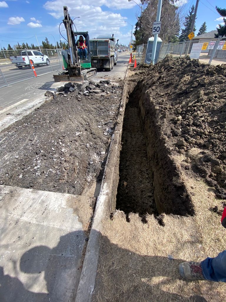 Excavator trenching alongside roadway with traffic control